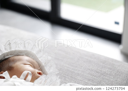 A newborn baby wearing a baby dress is sleeping by the window 124273704