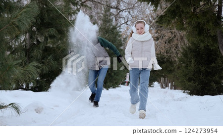 Young woman tossing snowball, laughing while sprinting through snow covered woodland during winter playfulness 124273954