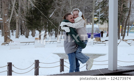 Young couple bonding during winter stroll, man playfully lifting girlfriend while sharing warm embrace and laughing amid snow covered landscape Young couple bonding during winter stroll, man playfully lifting girlfriend while sharing warm embrace and laughing amid snow covered landscape 124273974