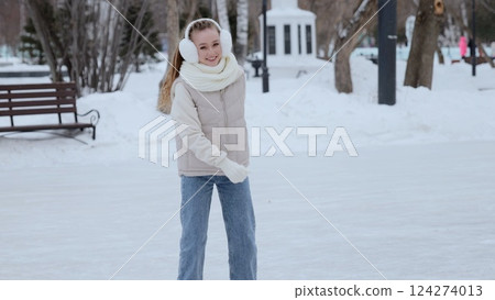 Teenage girl gliding confidently across icy rink, wearing warm winter outfit. Bright smile expressing pure happiness during seasonal outdoor skating experience 124274013