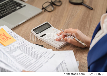 Business and Tax Management. An individual calculating tax figures with precision using a calculator amidst paperwork. Business and Tax Management. An individual calculating tax figures with precision using a calculator amidst paperwork. 124274636