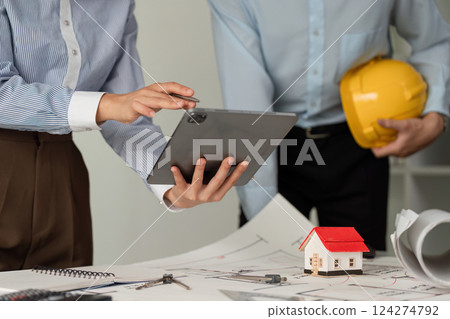 Collaboration and Construction Planning. Professionals discussing architectural plans while using a tablet for project management. Collaboration and Construction Planning. Professionals discussing architectural plans while using a tablet for project management. 124274792