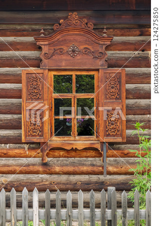 Intricately carved wooden window shutters and frame adorn a classic log cabin in russia, reflecting a photographer in the glass 124275850