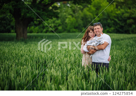 Loving parents cradling newborn amid golden wheat, sharing tender family connection under soft sunlight 124275854