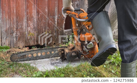 Logger starting old chainsaw near wooden wall Logger starting old chainsaw near wooden wall 124275986