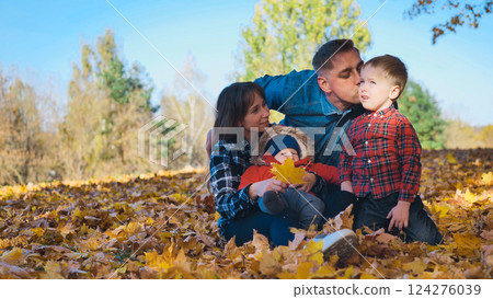Smiling family sitting on fallen leaves in a park during a beautiful autumn day, father kissing his son Smiling family sitting on fallen leaves in a park during a beautiful autumn day, father kissing his son 124276039