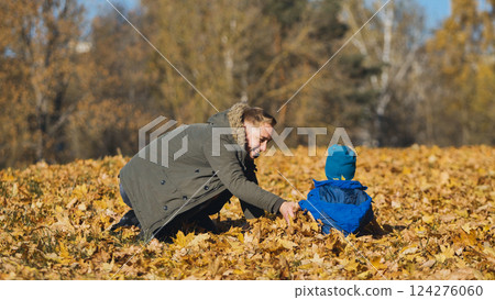 Father and son playing together, laughing amid golden autumn leaves, sunlight warming surrounding park landscape Father and son playing together, laughing amid golden autumn leaves, sunlight warming surrounding park landscape 124276060