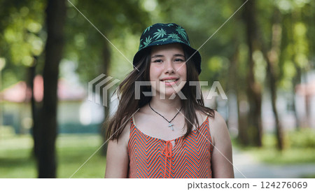 Teenage girl smiling, wearing cannabis leaf bucket hat, relaxing during sunny summer park day 124276069
