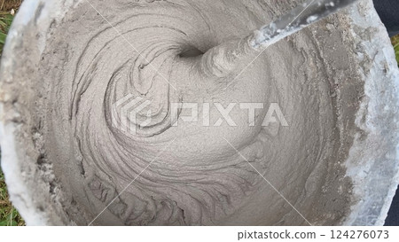 Construction worker mixing cement in bucket using mixing drill 124276073