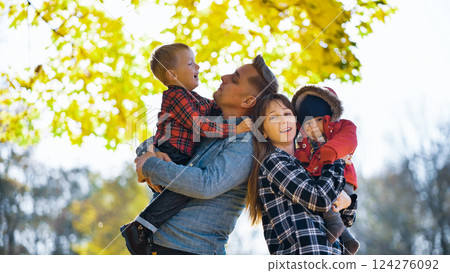 Parents holding their two sons, enjoying a sunny autumn day in a park, surrounded by colorful fall foliage Parents holding their two sons, enjoying a sunny autumn day in a park, surrounded by colorful fall foliage 124276092