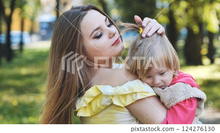 Young mother fixing her daughter's hair while carrying her in a city park during a sunny autumn day 124276130
