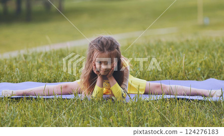 Flexible girl practicing gymnastic splits outdoors on yoga mat, showing her skills and enjoying healthy lifestyle Flexible girl practicing gymnastic splits outdoors on yoga mat, showing her skills and enjoying healthy lifestyle 124276183