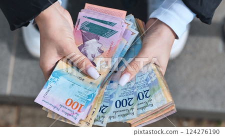 Woman showing a fan of venezuelan bolivar banknotes of different values, including 200 and 100, highlighting the country's currency Woman showing a fan of venezuelan bolivar banknotes of different values, including 200 and 100, highlighting the country's currency 124276190