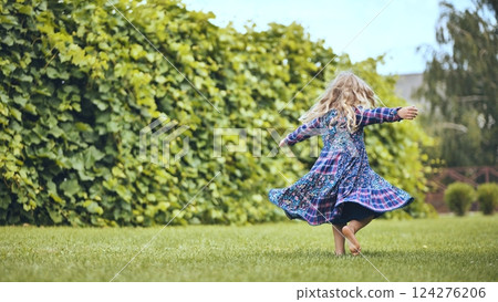 Young blonde girl spinning playfully in white sundress, dancing barefoot on lush green lawn near garden hedgerow, radiating childhood joy Young blonde girl spinning playfully in white sundress, dancing barefoot on lush green lawn near garden hedgerow, radiating childhood joy 124276206
