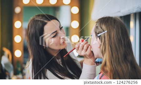 Professional makeup artist applying eyeshadow on young model near vanity mirror lights in studio makeup workspace Professional makeup artist applying eyeshadow on young model near vanity mirror lights in studio makeup workspace 124276256