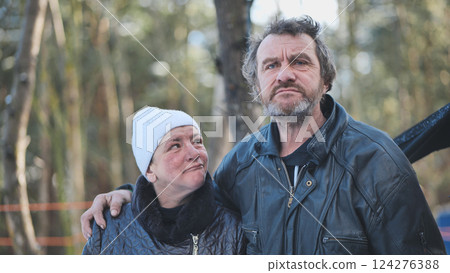 Alcohol addicted homeless couple stands together in a winter forest, facing an uncertain future with worry and despair 124276388