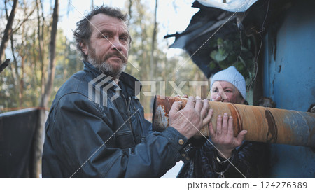 Homeless individuals clutching rusty pipe near makeshift shelter, symbolizing urban poverty and struggle for survival Homeless individuals clutching rusty pipe near makeshift shelter, symbolizing urban poverty and struggle for survival 124276389