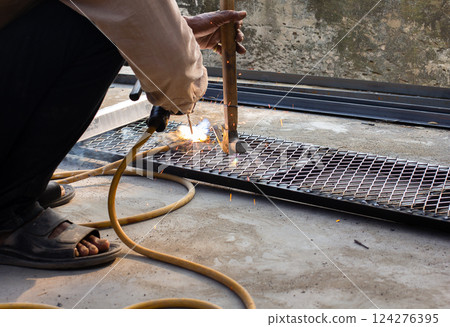 Welder is welding add joint at a construction site weld metal structures of Steel frames and grids for use in construction. Welder is welding add joint at a construction site weld metal structures of Steel frames and grids for use in construction. 124276395