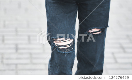 Close up of ripped black jeans on a girl walking on a paved street, showcasing urban style and fashion trends Close up of ripped black jeans on a girl walking on a paved street, showcasing urban style and fashion trends 124276439