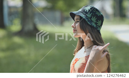 Teenage girl with bucket hat featuring marijuana leaf design enjoying a summer day in a park Teenage girl with bucket hat featuring marijuana leaf design enjoying a summer day in a park 124276462