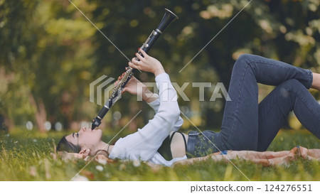 Young musician lying on grass in a park, playing clarinet and savoring the beauty of music intertwined with nature's tranquility 124276551