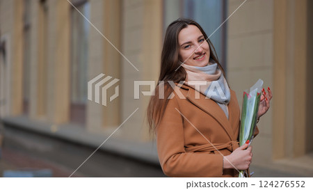 Portrait of a happy brunette girl with a tulip in the background of the city in the cold season. 124276552