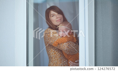 Mother embracing newborn near window, sharing tender bonding moment together 124276572