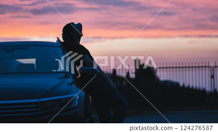 Relaxed woman silhouetted against car, resting during sunset after driving long highway stretch Relaxed woman silhouetted against car, resting during sunset after driving long highway stretch 124276587