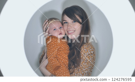 Smiling mother holding her newborn baby girl framed by a circle light, creating a tender and loving moment 124276595