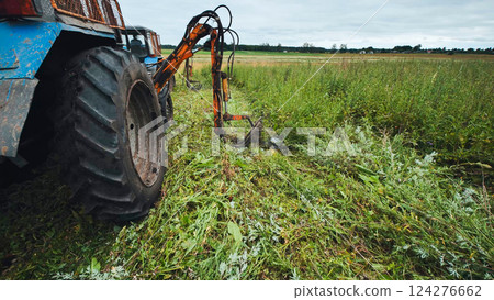 Tractor mowing grass with rotary mower on farmland 124276662