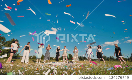 High school graduates joyfully throwing colorful confetti in the air during a summer field celebration 124276749