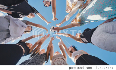 High school students standing in a circle with their hands raised towards a soccer ball under a clear blue summer sky 124276775