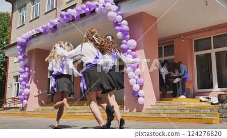 Excited graduates running out of school on last day, celebrating freedom under purple balloons. Childhood ends, new chapter begins. Sunny day, carefree fun with friends 124276820