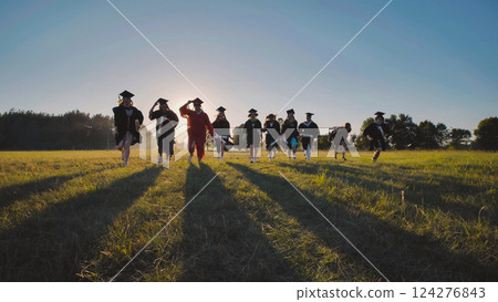 Group of cheerful graduates running together in a field at sunset, celebrating the end of high school Group of cheerful graduates running together in a field at sunset, celebrating the end of high school 124276843