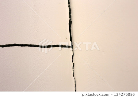 Close-up of a large crack running vertically and horizontally across an interior wall. 124276886