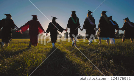 Group of graduates strolling through a field at sunset, hand in hand, celebrating their achievement Group of graduates strolling through a field at sunset, hand in hand, celebrating their achievement 124276951