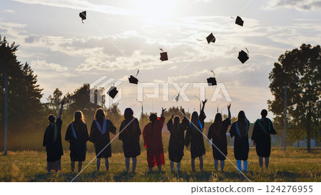 Students in academic gowns toss graduation caps into the air at sunset, celebrating their academic accomplishments as a group Students in academic gowns toss graduation caps into the air at sunset, celebrating their academic accomplishments as a group 124276955