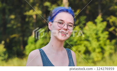 Smiling school student with blue hair, glasses, and braces posing in a natural outdoor setting 124276959