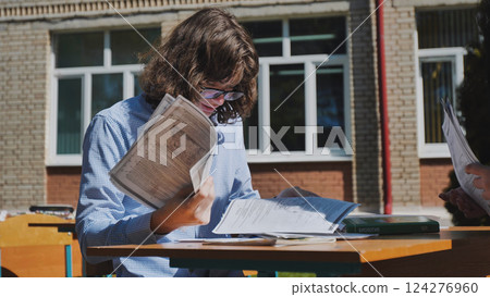 Concentrated teenage student reviewing test results at an outdoor school desk, diligently preparing for upcoming exams 124276960