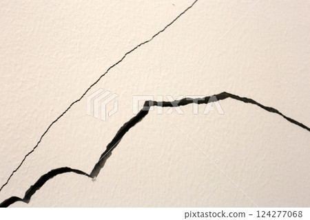 Close-up of a large crack running vertically and horizontally across an interior wall. 124277068