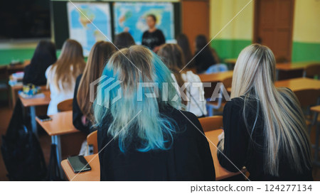 Students in a classroom listening to their teacher explain a geography lesson while sitting at their desks Students in a classroom listening to their teacher explain a geography lesson while sitting at their desks 124277134