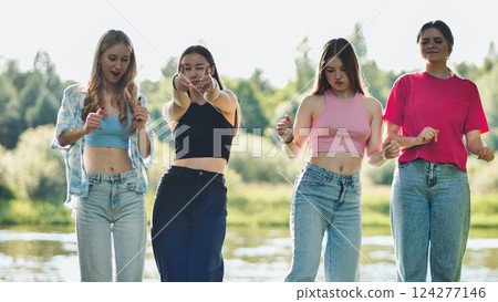 Four young women dancing joyfully by the river, soaking up the sun and celebrating friendship on a carefree summer day 124277146