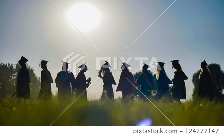 Silhouetted graduates walk in a field at sunset, holding their diplomas after the graduation ceremony Silhouetted graduates walk in a field at sunset, holding their diplomas after the graduation ceremony 124277147