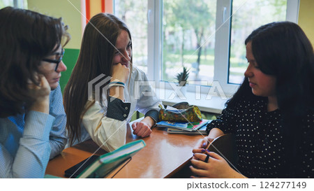 High school students and teacher engaged in discussion at desk in classroom during school day High school students and teacher engaged in discussion at desk in classroom during school day 124277149