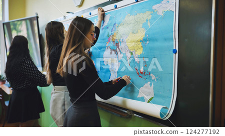 High school girls hanging a large world map on the blackboard, preparing for geography class, promoting education and teamwork High school girls hanging a large world map on the blackboard, preparing for geography class, promoting education and teamwork 124277192