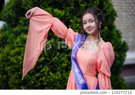Young woman wearing elegant peach dress and graduation sash, celebrating her academic achievement in 2024 Young woman wearing elegant peach dress and graduation sash, celebrating her academic achievement in 2024 124277218