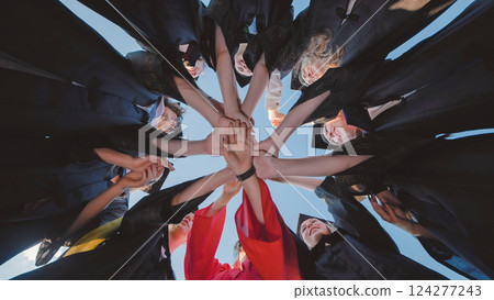 Graduates in academic gowns holding hands in circle, commemorating their academic success and the start of a new journey Graduates in academic gowns holding hands in circle, commemorating their academic success and the start of a new journey 124277243
