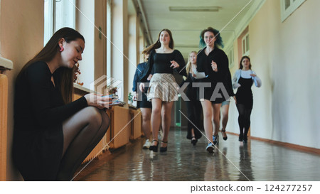 Lonely student reading a book, huddled in the school hallway as her peers dash by 124277257