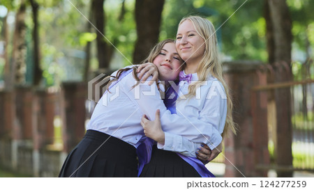 Two happy female students hugging tightly on their last school day. Wearing uniforms in a park on a sunny summer day 124277259