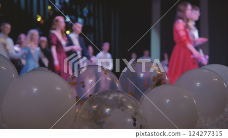 Jubilant graduates standing on stage, embracing amid vibrant balloons, marking academic milestone with shared excitement and pride Jubilant graduates standing on stage, embracing amid vibrant balloons, marking academic milestone with shared excitement and pride 124277315